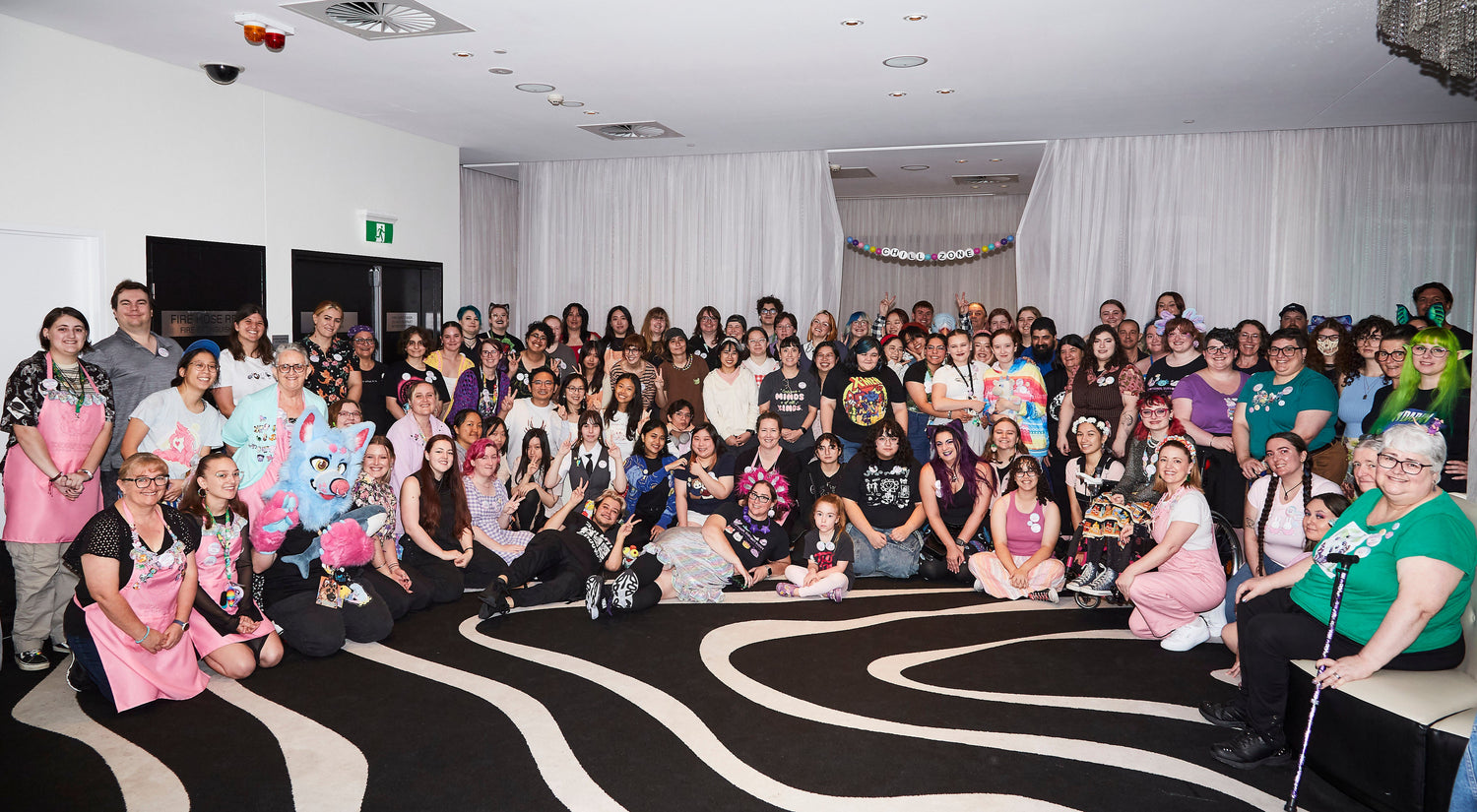 Large group of people posing for a photo in a room with a black and white patterned floor.