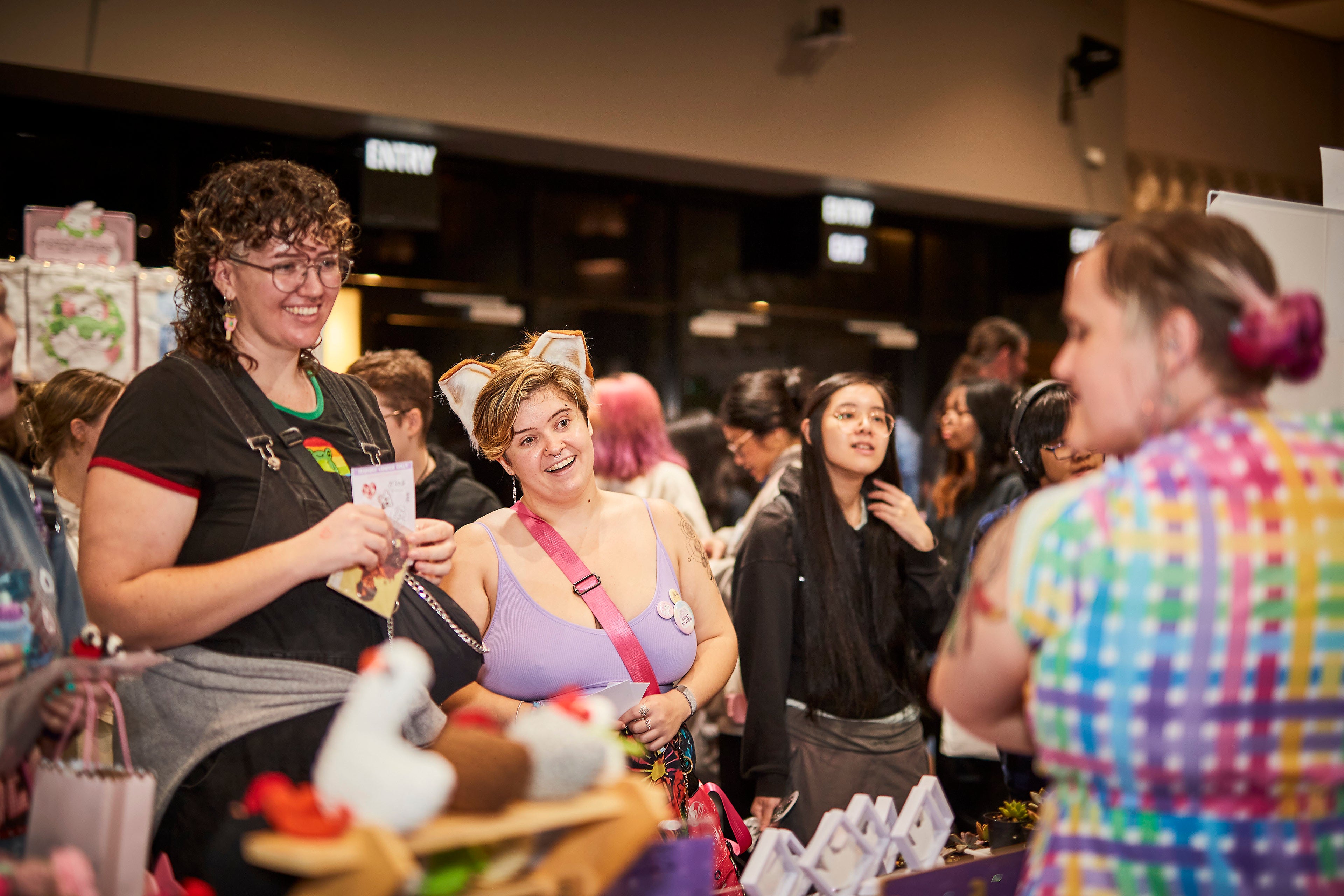 Woman in a black shirt holding a card in a crowded room with people and booths.