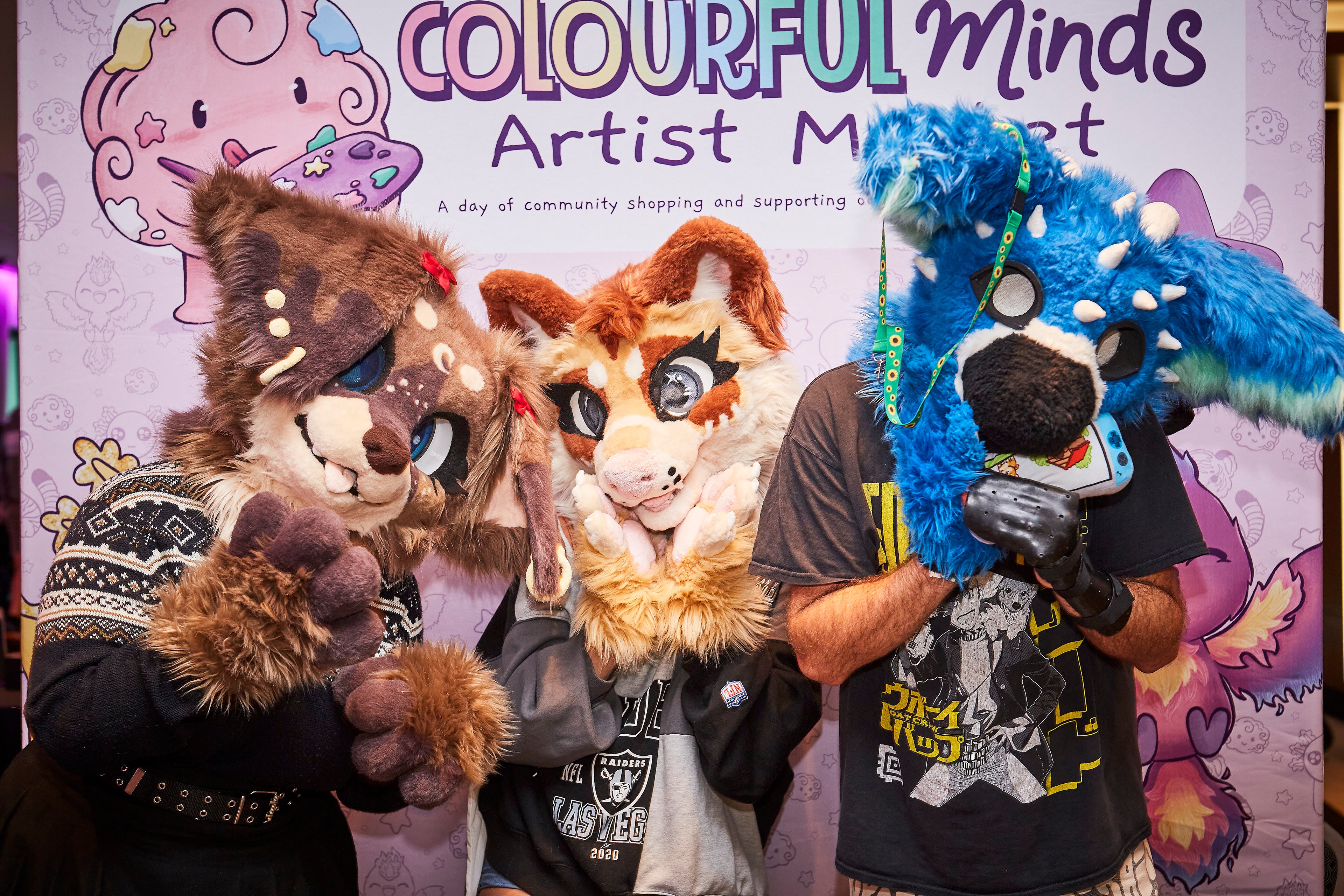 Three people in animal costumes standing in front of a colorful backdrop with 'Colourful Minds' branding.