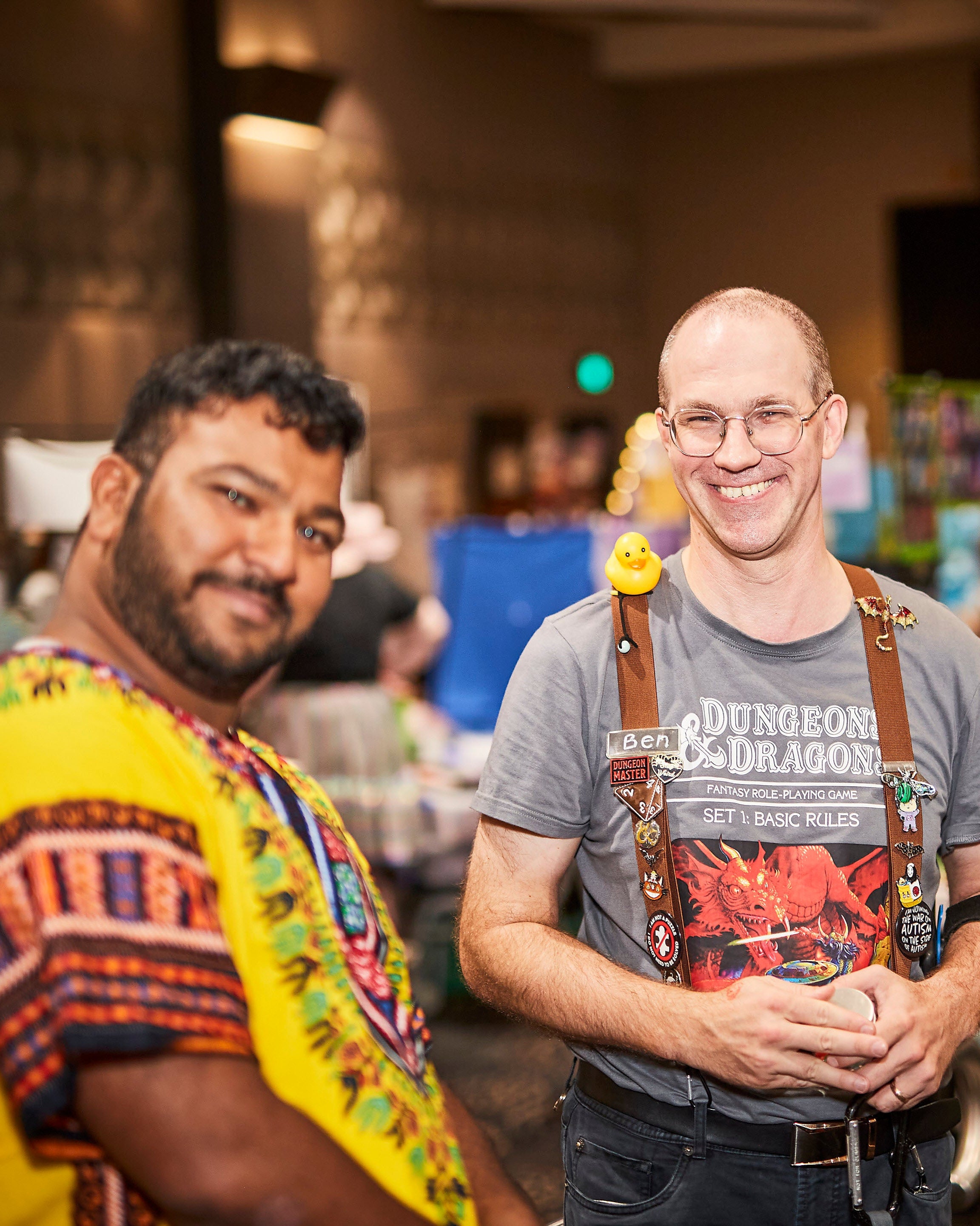 Two men standing in a convention center with a table and people in the background